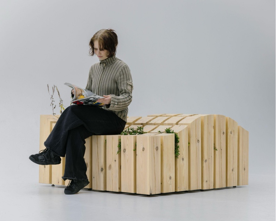 Studiossa otettu tuotekuva kasveja sisältävästä penkkikalusteesta, jonka päällä istuu henkilö lukemassa lehteä.