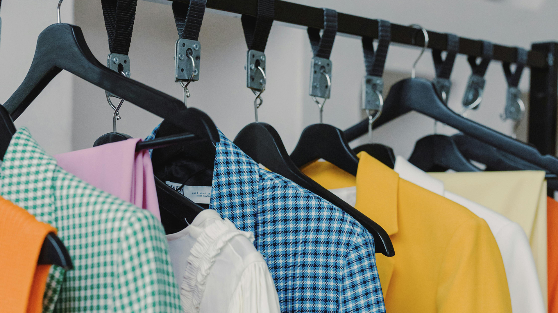 Värikkäitä vaatteita roikkuu henkareissa vaaterekillä.