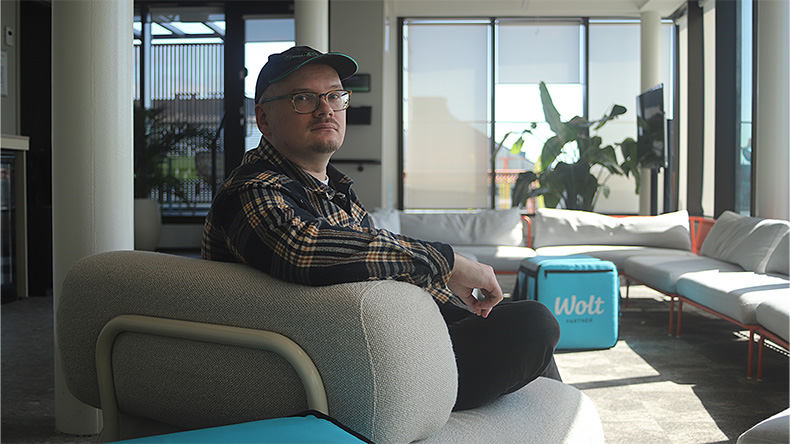 Risto Flink istuu toimiston nojatuolilla ja katsoo kameraan. Taustalla näkyy Woltin kylmälaukku, isoja huonekasveja ja toimiston sohvia.