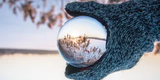 A hand holding a glass ball in a winter landscape