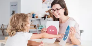 nainen näyttää lapselle paperilappuja, joissa on iloinen ja surullinen naama