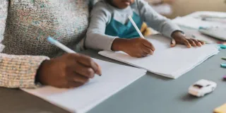 Nainen ja lapsi istuvat pöydän ääressä ja kirjoittavat