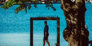 Mies kävelee koiransa kanssa Lappeenranta kehyksen ohitse Saimaan rannalla