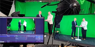 Vihreän taustakankaan edessä kaksi miestä keskustelemassa studiossa 