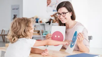 nainen näyttää lapselle paperilappuja, joissa on iloinen ja surullinen naama