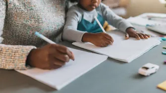 Nainen ja lapsi istuvat pöydän ääressä ja kirjoittavat