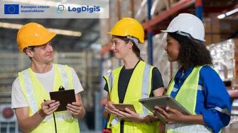 kolme ihmistä varastohallissa kypärät päässä ja suojaliivit päällä neuvottelemassa