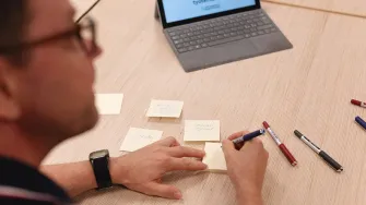 Mies kirjaa muistilapulle asioita työpöydän ääressä