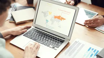 Ihmisiä kokouspöydän äärellä, mies katsoo läppärin näyttöä