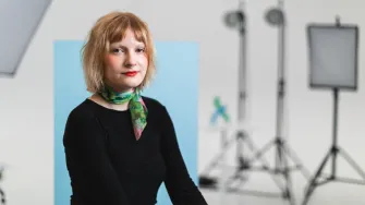 Kuvassa valokuvauksen opiskelija Viivi Päiväsaari istuu Muotoiluinstituutin valokuvastudiossa kuvauskaluston ympäröimänä