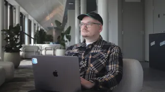 Risto Flink istuu toimiston nojatuolissa kannettava tietokone sylissään. Taustalla näkyy isoja huonekasveja.