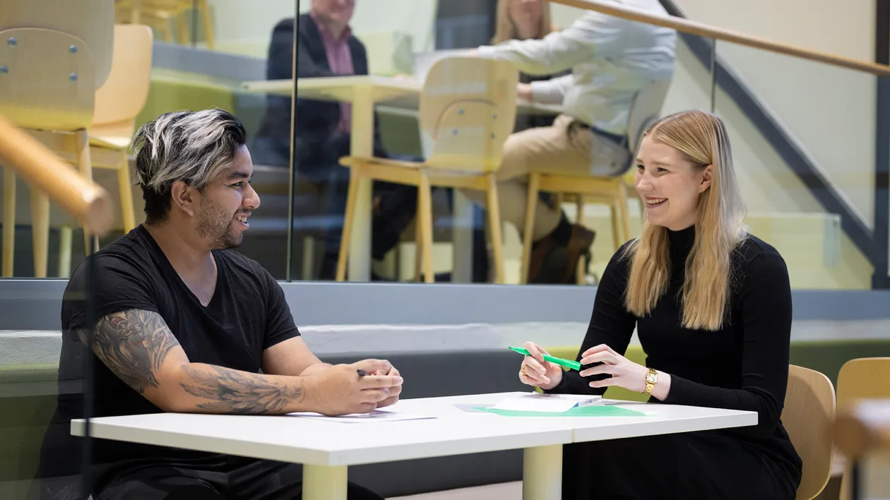 Opiskelijat istuvat pöydän ääressä ja hymyilevät toisilleen.