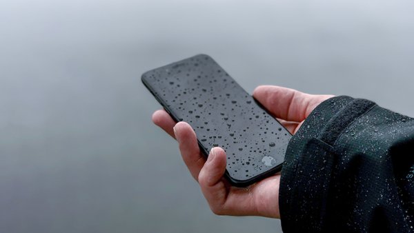 A hand holding a mobile phone in the rain