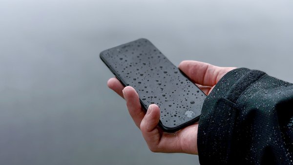 A hand holding a mobile phone in the rain 