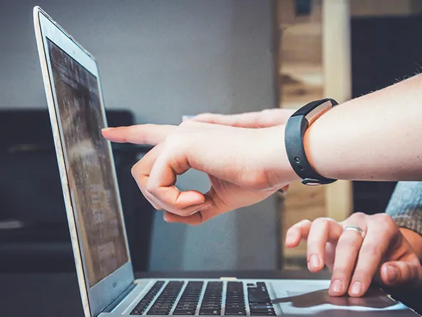 Käsiä osoittamassa kannettavaa tietokonetta.