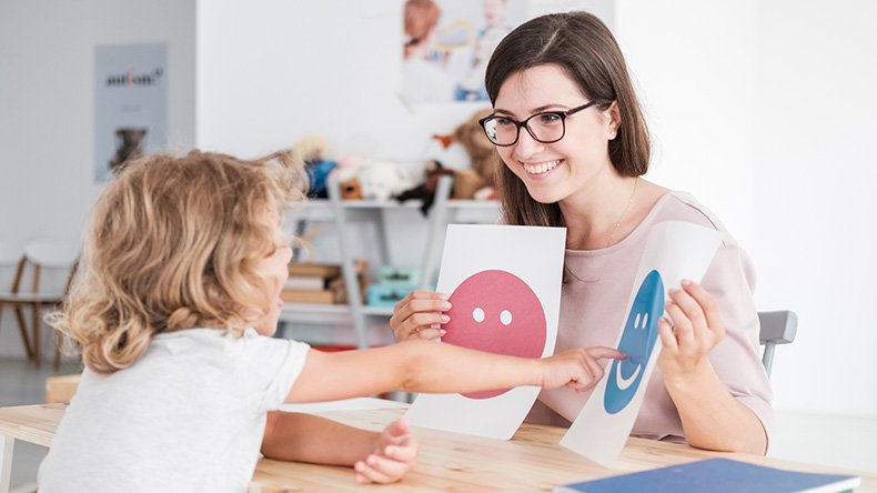 nainen näyttää lapselle paperilappuja, joissa on iloinen ja surullinen naama