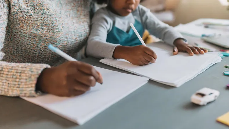 Nainen ja lapsi istuvat pöydän ääressä ja kirjoittavat