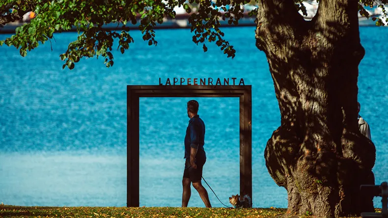 Mies kävelee koiransa kanssa Lappeenranta kehyksen ohitse Saimaan rannalla