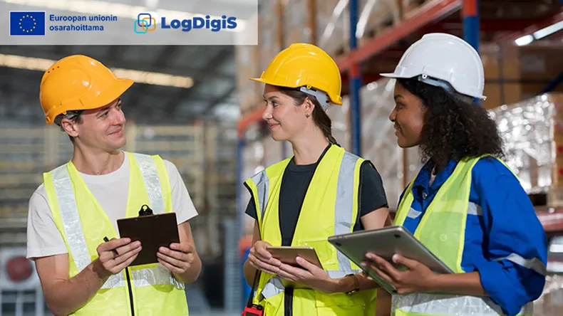 kolme ihmistä varastohallissa kypärät päässä ja suojaliivit päällä neuvottelemassa