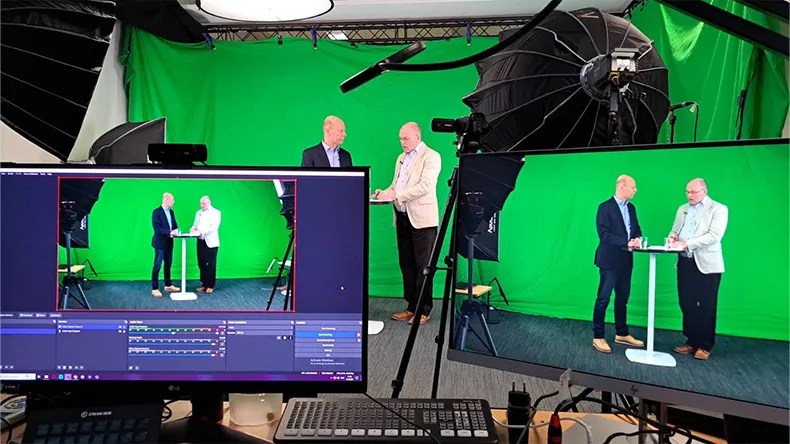 Vihreän taustakankaan edessä kaksi miestä keskustelemassa studiossa 