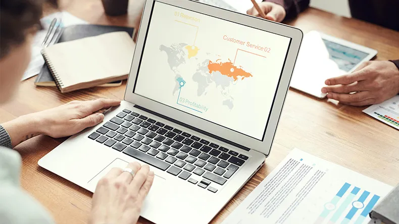 Ihmisiä kokouspöydän äärellä, mies katsoo läppärin näyttöä