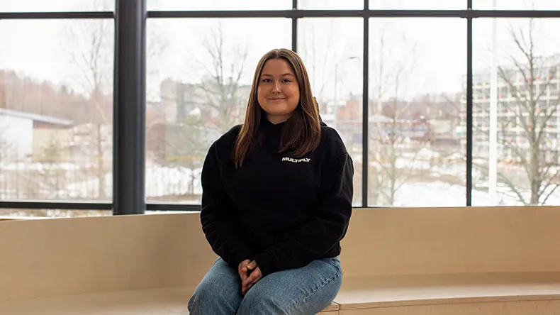 Tradenomiopiskelija Iida Leinonen penkillä taustallaan ikkunasta avautuva talvinen maisema. 