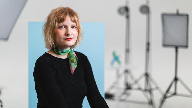 Kuvassa valokuvauksen opiskelija Viivi Päiväsaari istuu Muotoiluinstituutin valokuvastudiossa kuvauskaluston ympäröimänä