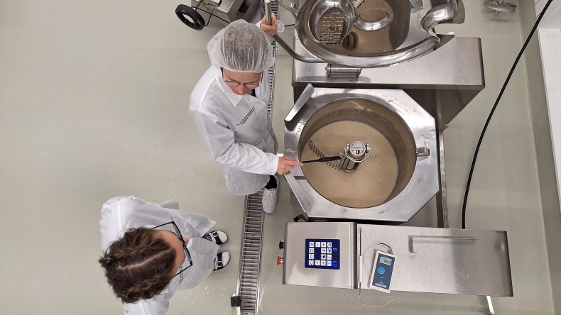 Kaksi laboratoriotyöntekijää suurtalouskattilan ääressä valmistamassa kauratuotetta