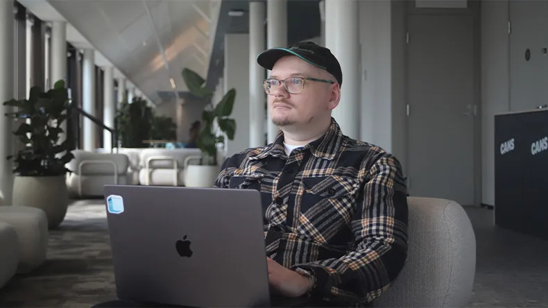 Risto Flink istuu toimiston nojatuolissa kannettava tietokone sylissään. Taustalla näkyy isoja huonekasveja.